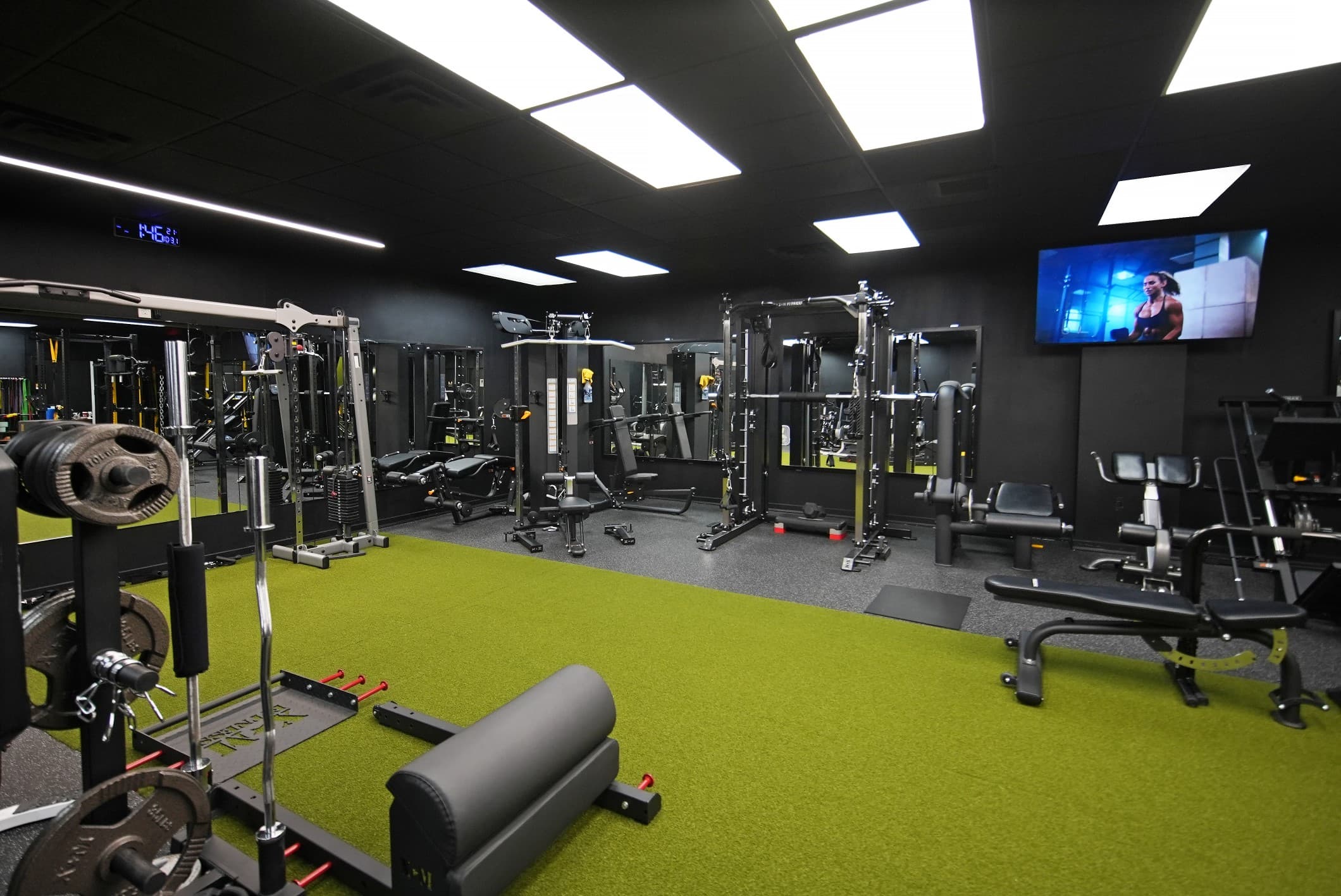 The training floor at Trusted Sport Club: black walls, green turf, racks and machines
